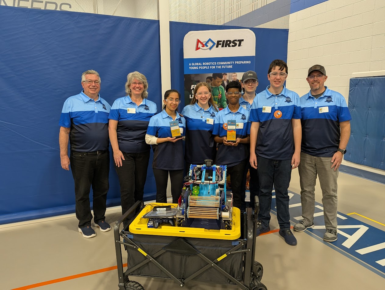 The Bionic Sharks FTC Team 19541 holding a $2,000 Monumental Impact grant check beside their competition robot
