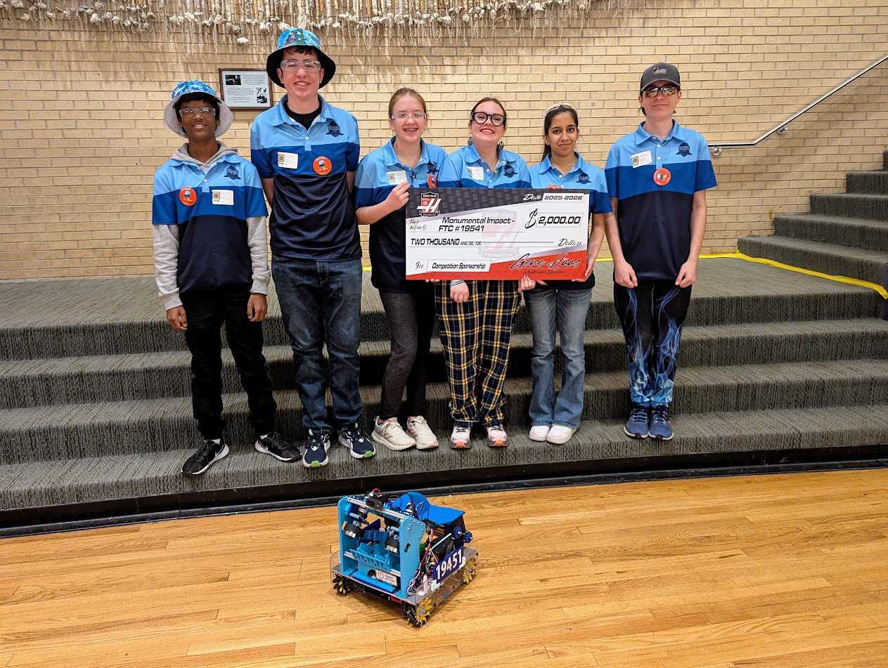 The Bionic Sharks FTC Team 19541 holding a $2,000 Monumental Impact grant check beside their competition robot